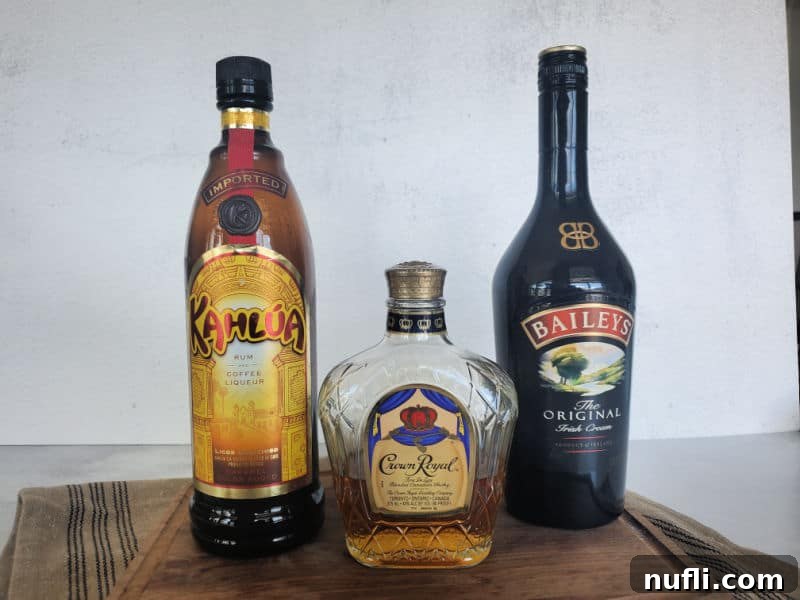 Bottles of Kahlua Coffee Liqueur, Crown Royal Canadian Whiskey, and Bailey's Irish Cream arranged on a wooden surface, highlighting the core ingredients of a Duck Fart Shot.