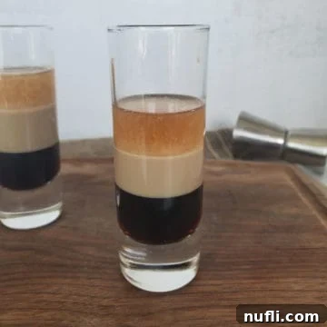 Duck Fart Shot layered in a shot glass sitting on a wood cutting board with a cocktail jigger