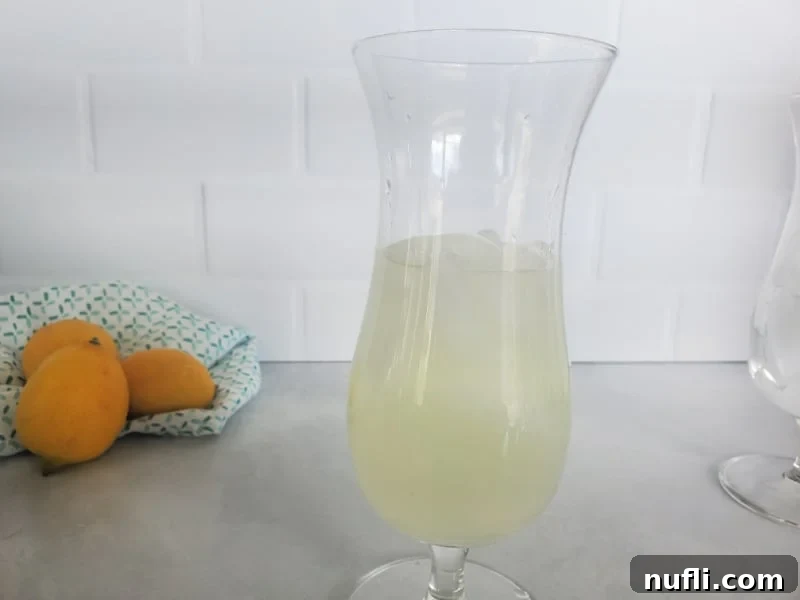 A hurricane glass filled with ice and lemonade, with fresh lemons in the background.