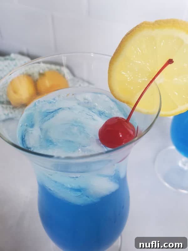 Close-up, looking down into a finished Blue Lagoon Cocktail garnished with a maraschino cherry and a lemon wheel.