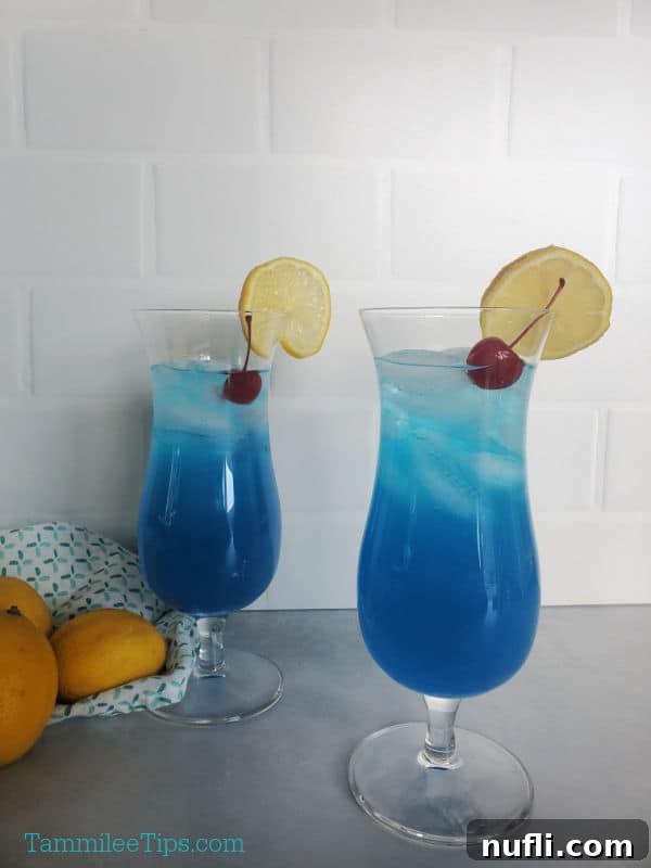 Two vibrant blue Blue Lagoon drinks in hurricane glasses, garnished with a maraschino cherry and a lemon wheel.