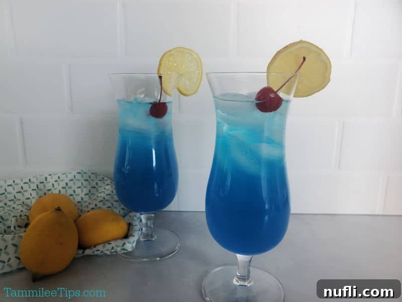 Two beautifully presented Blue Lagoon Cocktails in hurricane glasses, garnished with maraschino cherries and lemon wheels.