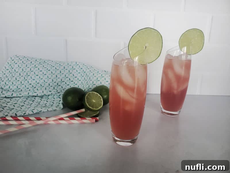 The third step of making a Bay Breeze cocktail: pouring cranberry juice into a highball glass to create layers, with a finished Bay Breeze cocktail behind it and a cocktail jigger.