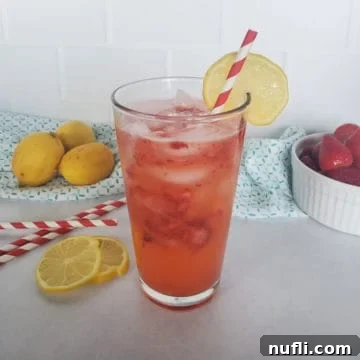 A glass of homemade Freckled Lemonade, featuring crushed strawberries and a lemon wheel garnish, invitingly presented.