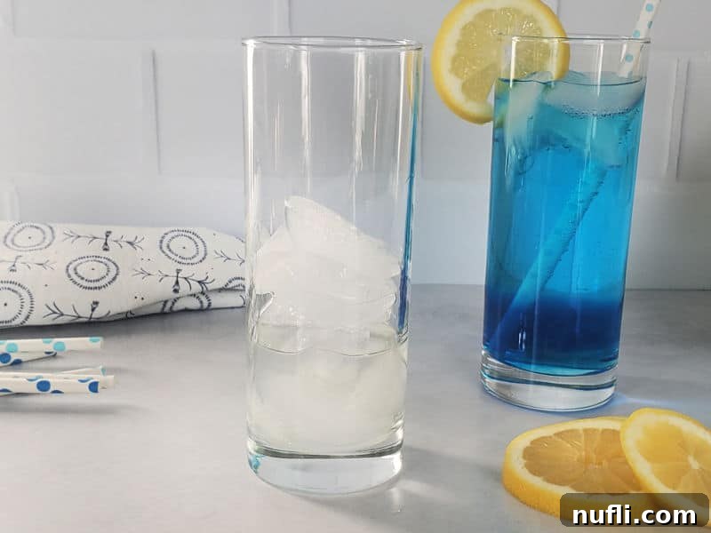 Shake Up the Sex in the Driveway: Video Cocktail Recipe 4 An empty highball glass filled with ice cubes sits next to a finished blue cocktail with a lemon wheel, ready for the next step.