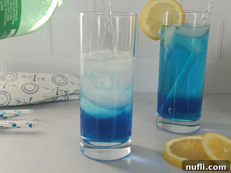 Clear liquid pouring from a Sprite bottle into a glass with blue liquid sitting next to a blue cocktail and lemon wheels