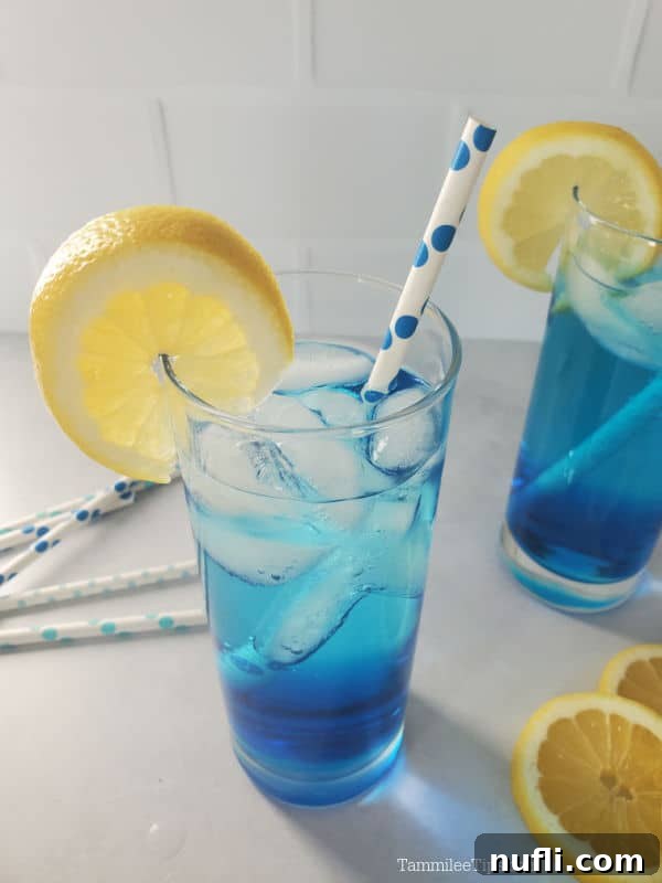 Looking down on a blue drink with a lemon wheel garnish and paper straw