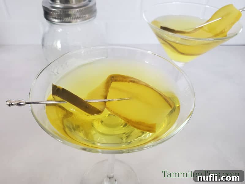 Pickle martini with a pickle garnish next to a cocktail shaker