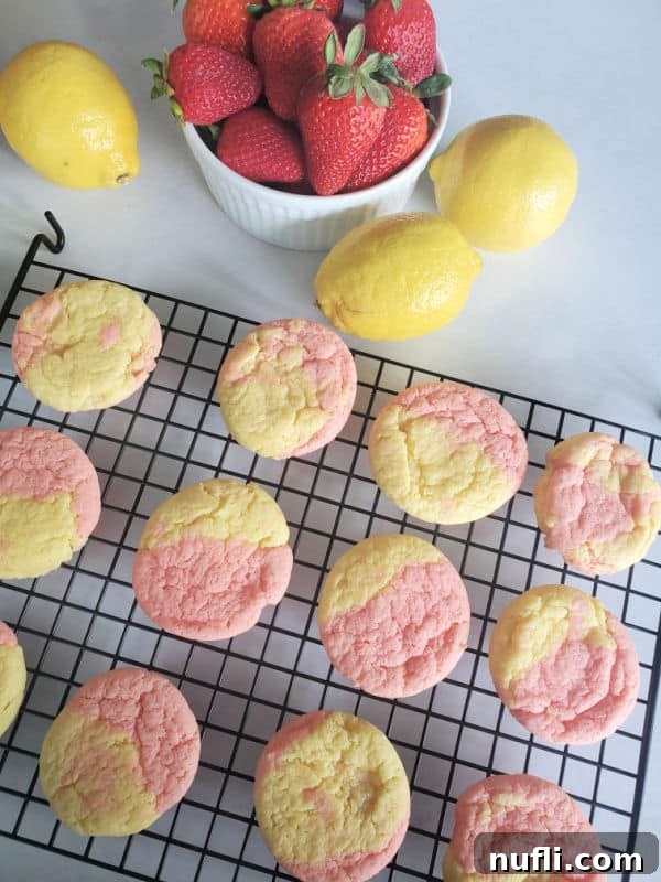 Freshly baked strawberry lemonade cookies on a wire rack, accompanied by a bowl of fresh strawberries and lemons.