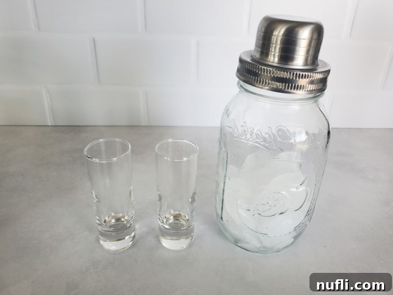 Two clear glass shot glasses with a mason jar cocktail shaker 