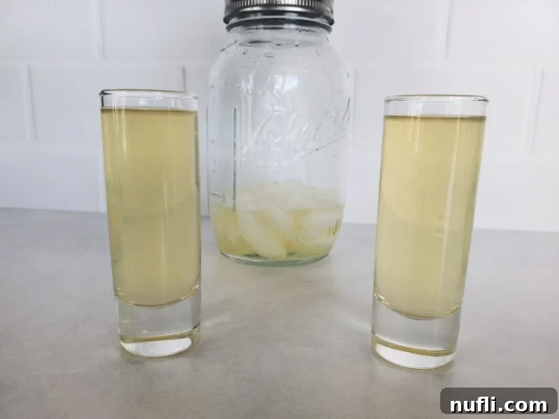 Two Green Tea Shots in clear glass shot glasses with a mason jar cocktail shaker behind them. 