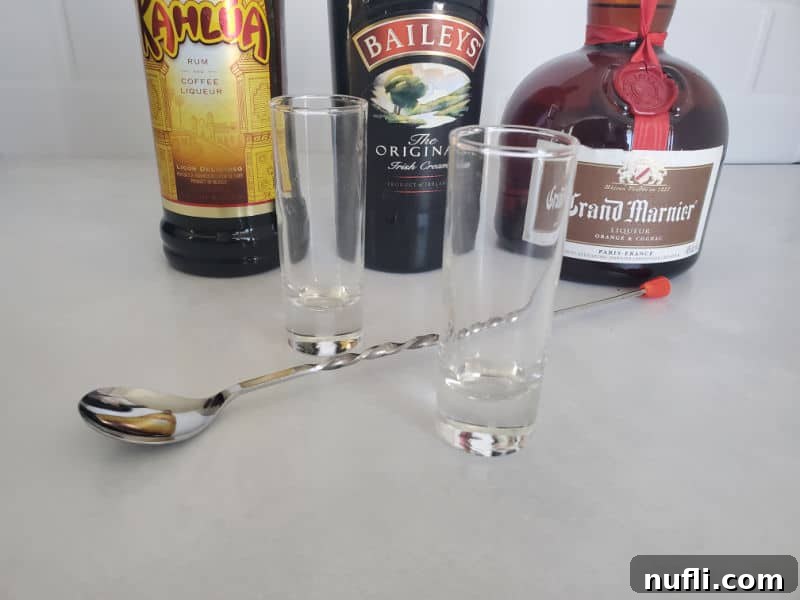 Crafting the B52 Shot A Video Guide 4 Kahlua, Bailey's Irish Cream, and Grand Marnier bottles alongside two shot glasses and a bartending spoon, poised for making a B52 shot.