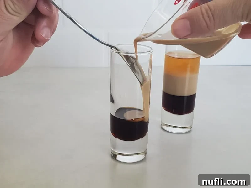 Crafting the B52 Shot A Video Guide 6 Bailey's Irish Cream being slowly poured over a layer of Kahlua using a bar spoon, next to a completed B52 shot.