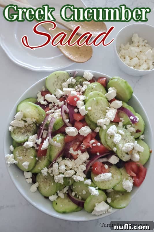 Freshly prepared Greek Cucumber Salad on a white plate, garnished with feta cheese, alongside a bowl of extra feta and wooden serving spoons.