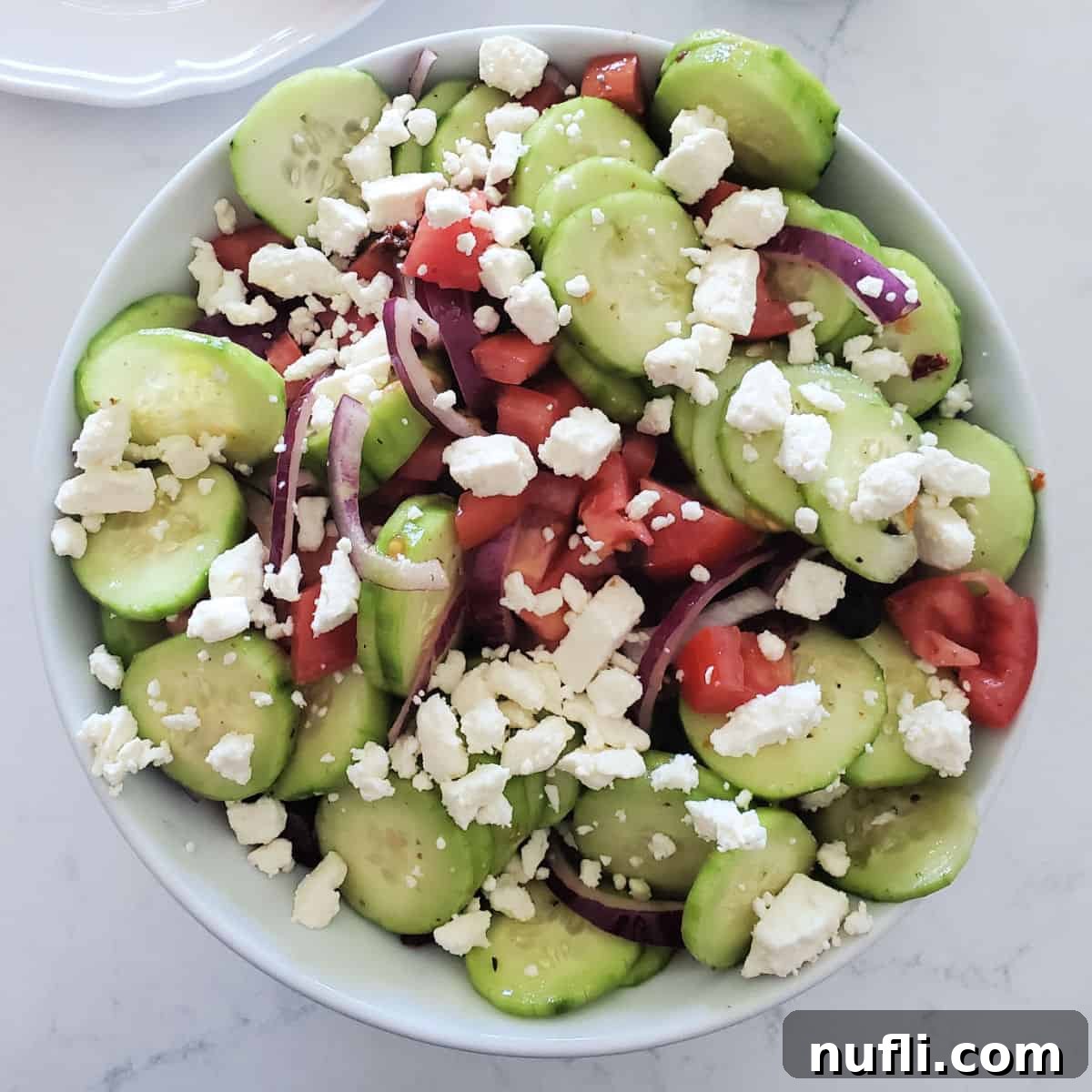 A large white bowl of Greek Cucumber Salad with crumbled feta cheese on top, ready to serve.
