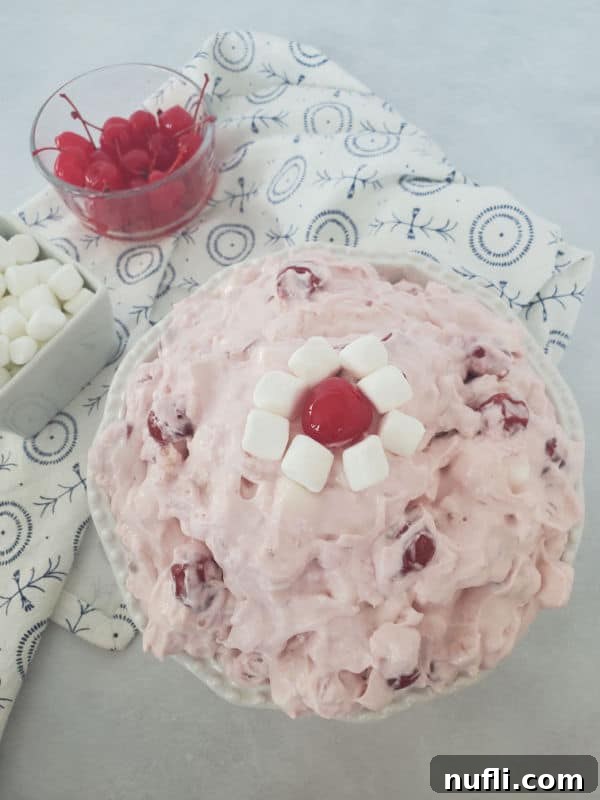Cherry Fluff cool whip salad in a white bowl next to a bowl of mini marshmallows and a bowl of cherries