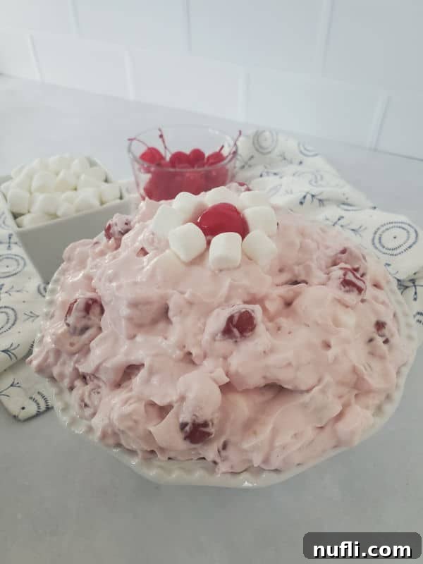 Cherry cool whip salad in a white bowl next to bowls with cherries and mini marshmallows in them.
