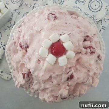 Cherry fluff salad in a white bowl garnished with mini marshmallows and a maraschino cherry
