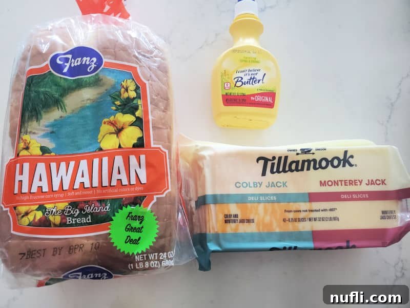 Ingredients for air fryer grilled cheese: Hawaiian bread, butter spray, and a package of Tillamook sliced cheese on a wooden board