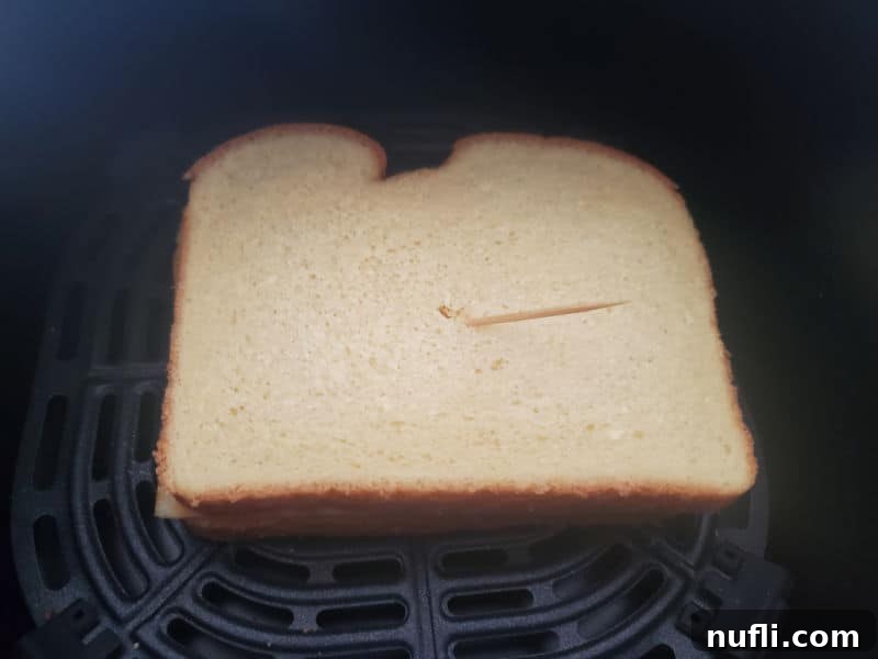 Grilled cheese sandwich in an air fryer basket, held together with a toothpick to prevent the top slice from blowing off