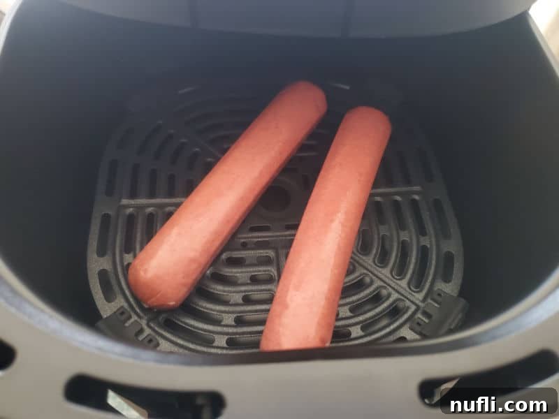 Two hot dogs perfectly placed in an air fryer basket, ready for cooking to achieve a crispy exterior.