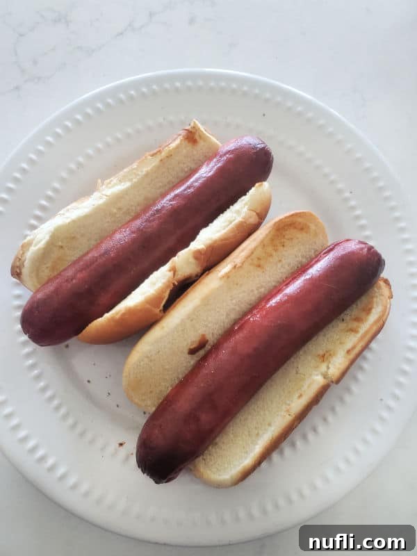 A delicious plate featuring two air-fried hot dogs, each placed in a perfectly toasted bun, served on a clean white plate.