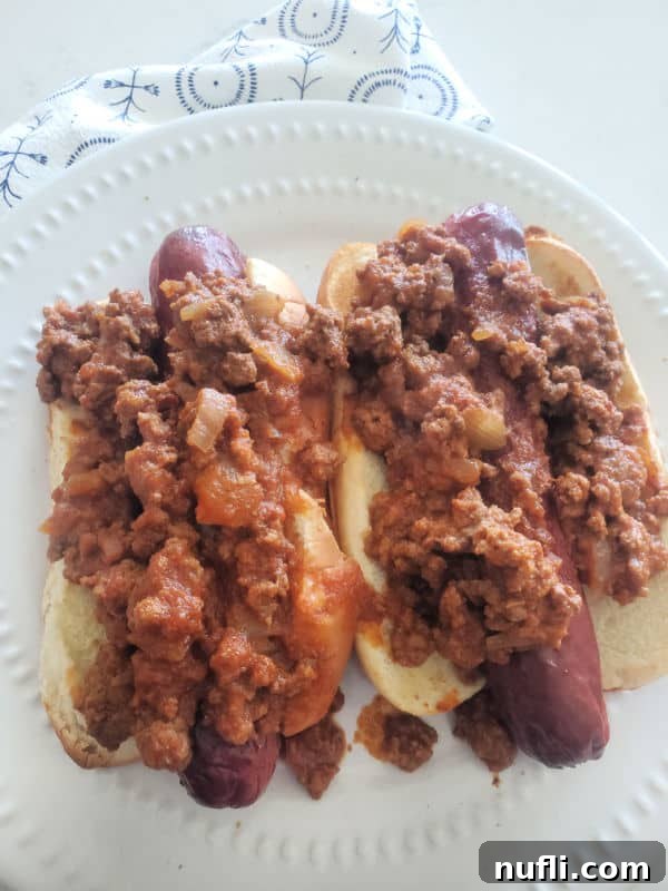 two chili dogs with homemade hot dog chili over them on a white plate