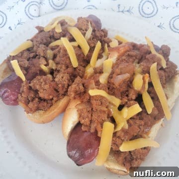 two chili dogs covered in homemade hot dog chili on a white plate