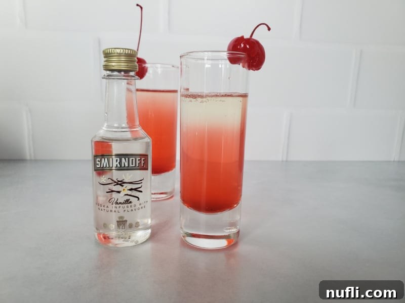 two Pineapple upside down cake shots with cherry garnish next to a bottle of smirnoff vanilla vodka 