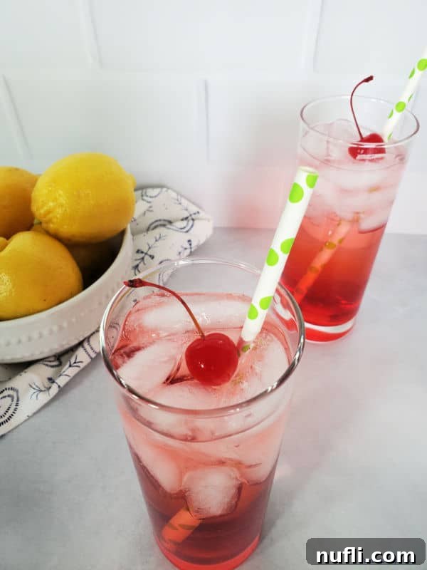 Overhead view of two Dirty Shirley Drinks, garnished with maraschino cherries and paper straws, alongside a bowl of fresh lemons.