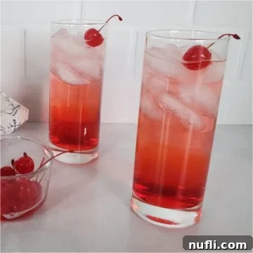 Two red cocktails in tall glasses garnished with maraschino cherries next to a bowl of cherries