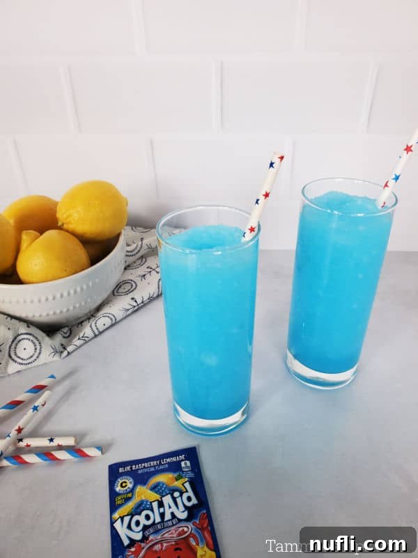 two bright blue kool aid slushies in tall glasses with paper straws, near a bowl of lemons and a package of Kool-Aid
