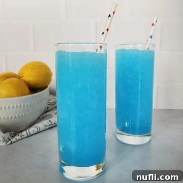 two bright blue kool aid slushies in tall glasses with paper straws, near a bowl of lemons