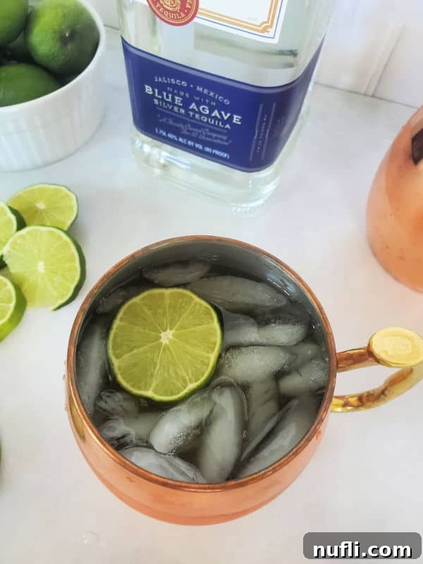 Mexican mule cocktail in a copper mug with a lime slice next to a bottle of tequila and additional lime slices