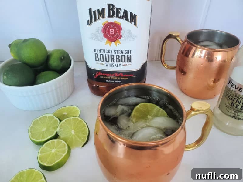 The Best Easy Kentucky Mule Recipe 4 A perfectly mixed Kentucky Mule in a gleaming copper mug, surrounded by a bottle of Jim Beam Bourbon, a bottle of refreshing ginger beer, and a scattering of fresh lime wheels.