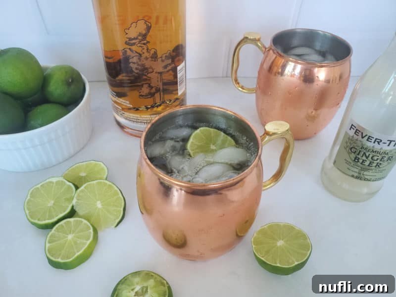 The Best Easy Kentucky Mule Recipe 5 A refreshing Kentucky Mule cocktail in a chilled copper mug, garnished with a lime slice. A bottle of bourbon and a bottle of ginger beer are visible in the background.