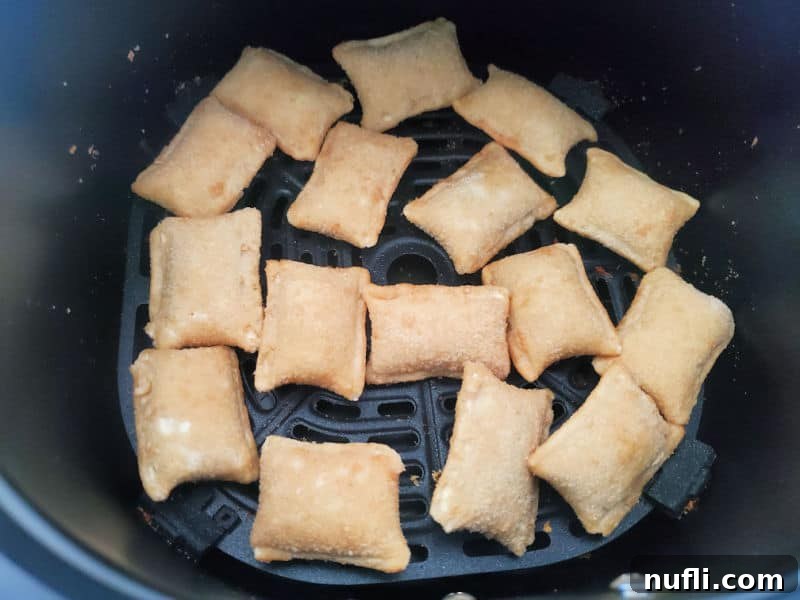 Frozen pizza rolls laid out in a single layer inside an air fryer basket.