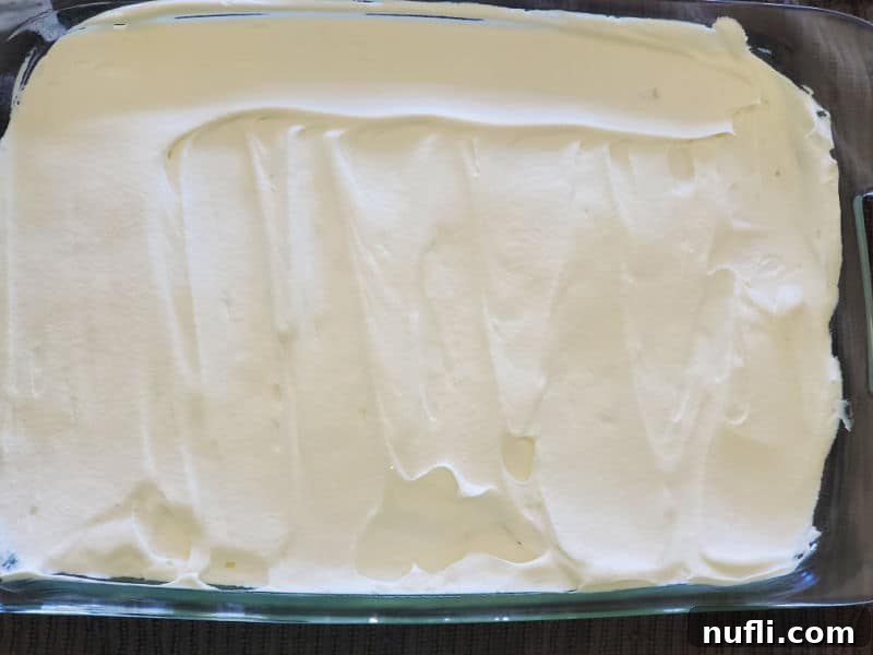Whip cream spread evenly across a cake in the baking dish