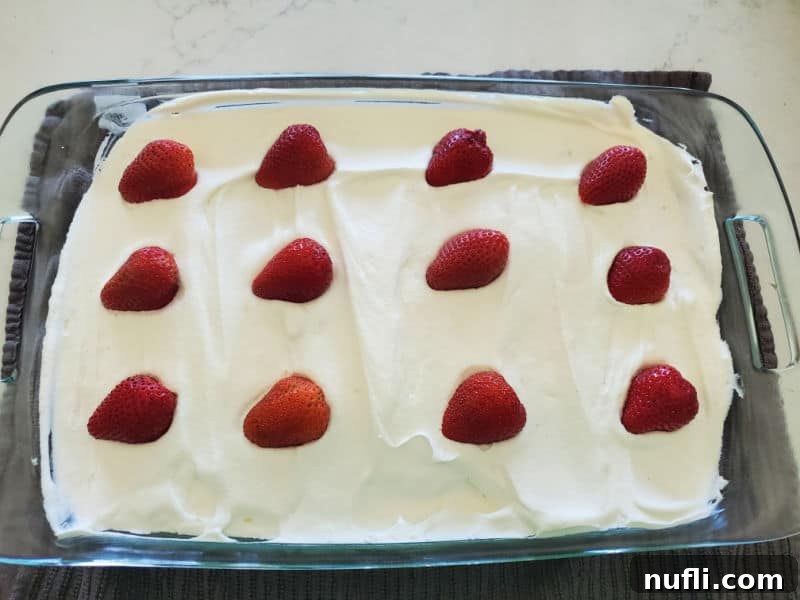Cut strawberries lined up on whipped topping in a baking dish