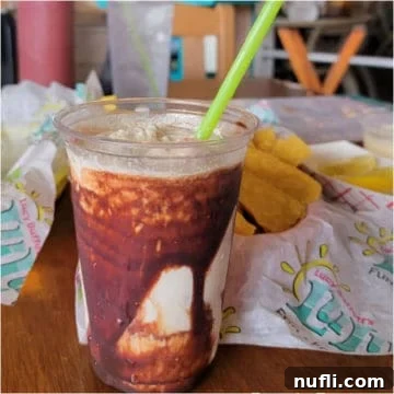 Chocolate bushwacker in a plastic cup with a green straw, lulu's chips and salsa next to the glass