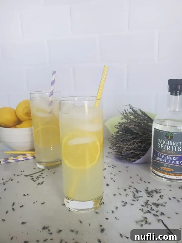 Lavender Lemonade Cocktails in tall glasses with lemon slices next to a bottle of Oakhurst Spirits Lavender Vodka and a bundle of Lavender.