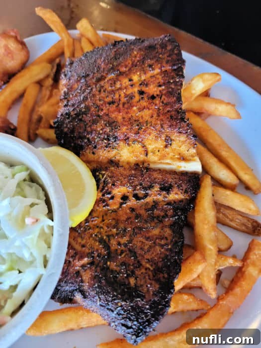 A plate of blackened Mahi Mahi on a bed of crispy French Fries, accompanied by creamy Coleslaw at LuLu's Gulf Shores.