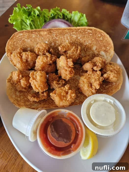 Delicious shrimp po'boy sandwich on a white plate with condiments and fresh vegetables