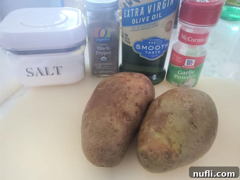 Fresh Russet potatoes, olive oil, garlic powder, salt, and pepper arranged on a rustic cutting board, ready for prep.