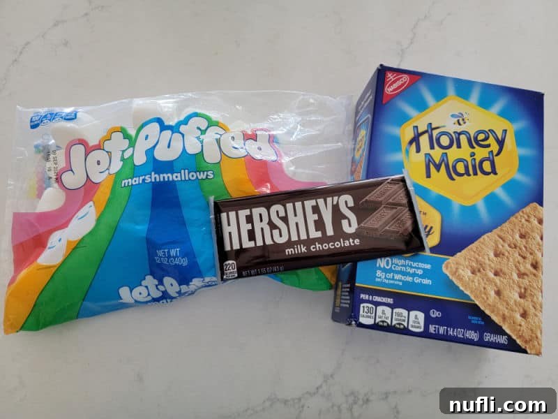 Gooey Air Fryer Smores 3 Classic S'mores ingredients artfully arranged on a clean white counter: Jet Puffed Marshmallows bag, Hershey's Chocolate Bar, and Honey Maid graham crackers box.