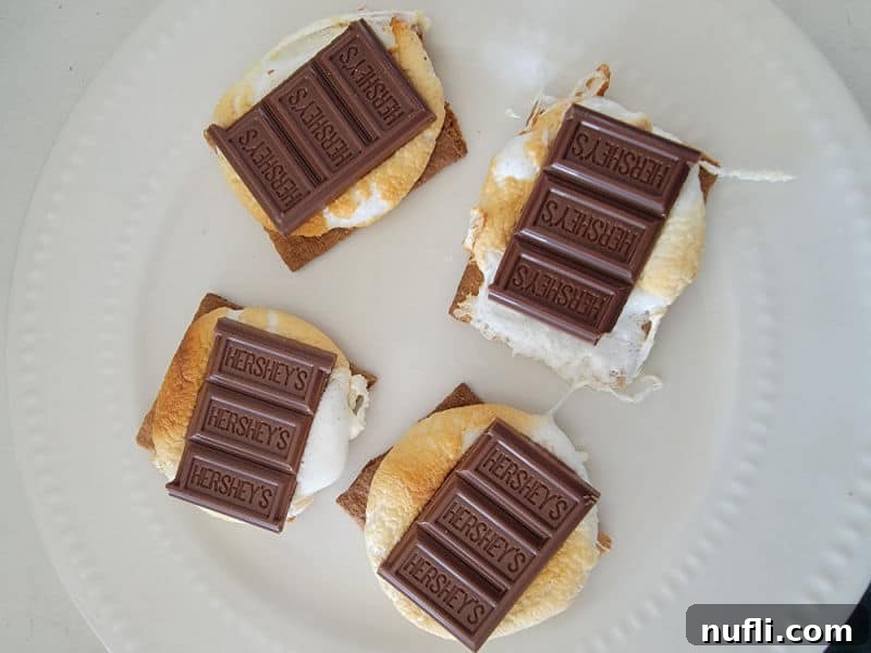 Gooey Air Fryer Smores 7 A freshly assembled s'more on a white plate, featuring a perfectly squished, golden marshmallow topped with a melted Hershey's chocolate square and the other half of a graham cracker.