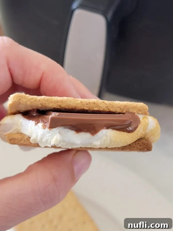 Gooey Air Fryer Smores 8 A close-up shot of a hand holding a freshly made s'more, showcasing the perfectly melted chocolate and toasted marshmallow between graham crackers.
