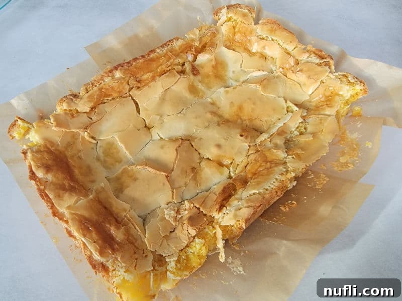 A close-up of Gooey Butter Cake slices on parchment paper, showing the soft, chewy texture.