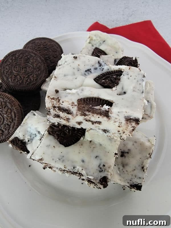 Easy 3-Ingredient Oreo Fudge 4 Perfectly cut squares of 3-ingredient Oreo fudge are arranged artfully on a white plate, with whole Oreo cookies serving as a delicious backdrop.