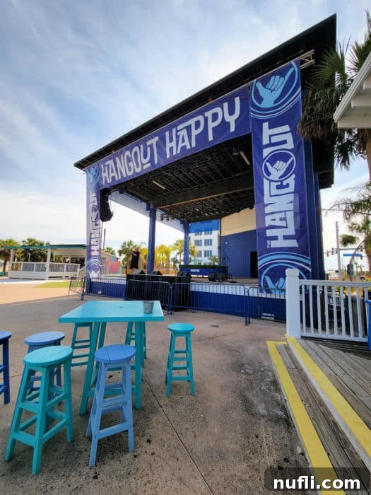 Outdoor stage at The Hangout with 'Hangout Happy' banner, surrounded by tables and chairs